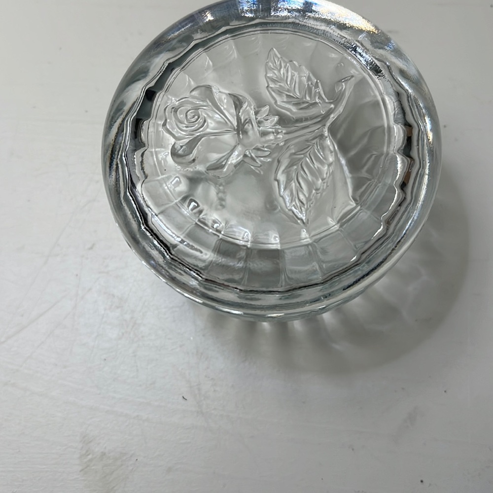 Small round glass container with lid. Rose on top.